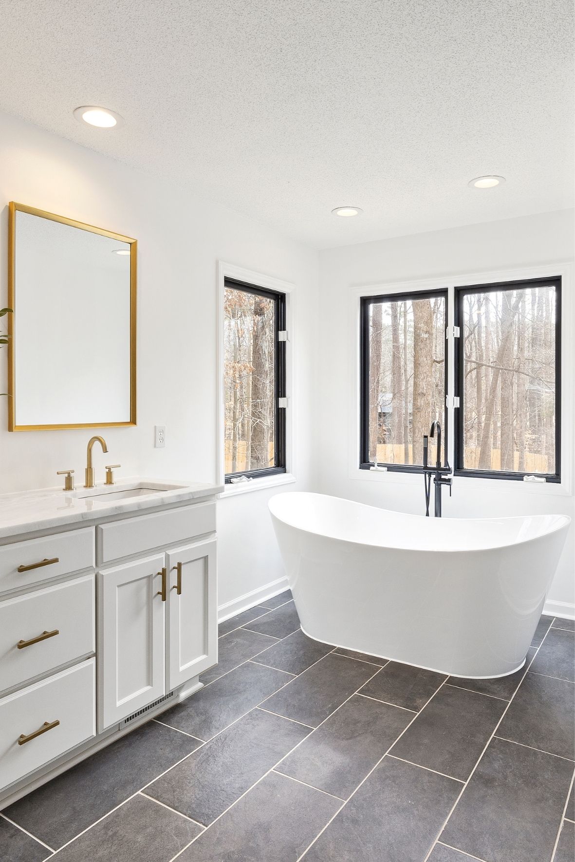 Salle de bain lumineuse avec baignoire autoportante, meuble blanc et grandes fenêtres au cadre foncé  à Mont-Tremblant