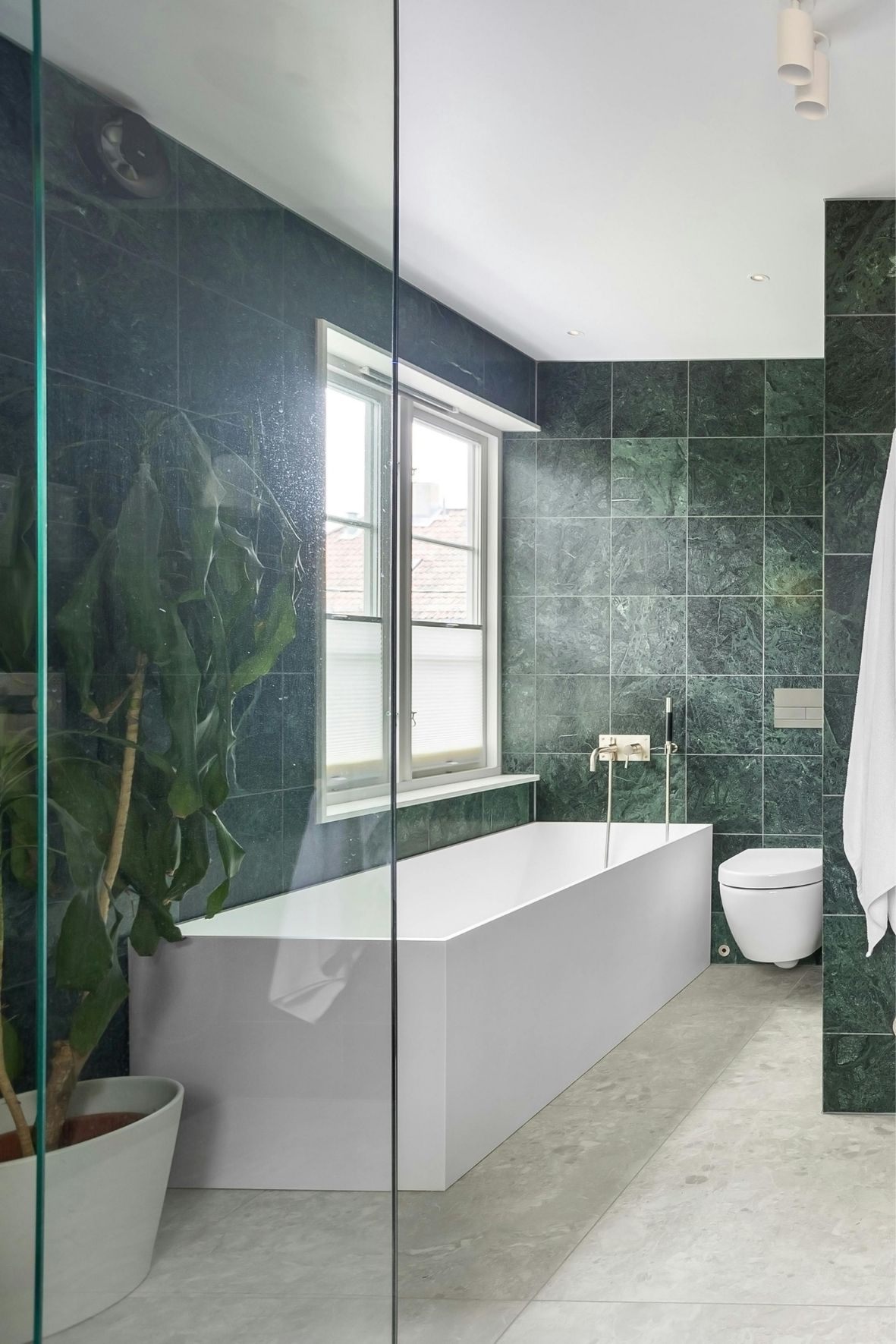 Salle de bain avec baignoire encastrée, WC suspendu, murs carrelés verts et sol clair  à Sainte-Julie